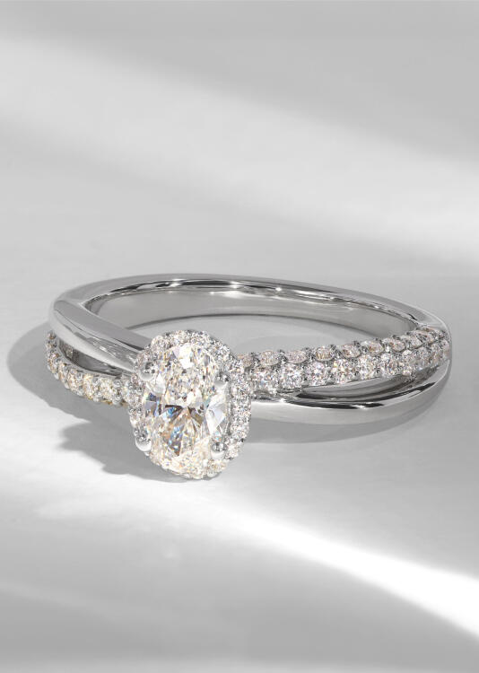 A diamond halo engagement ring in white gold with intersecting shanks of smooth gold and diamonds.
