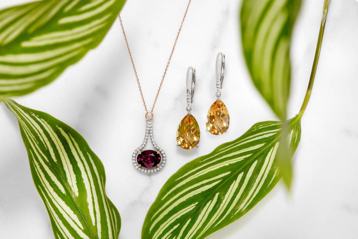 Citrine gemstone earrings on a white background to the right of a pendant made of purple garnet and diamonds. 