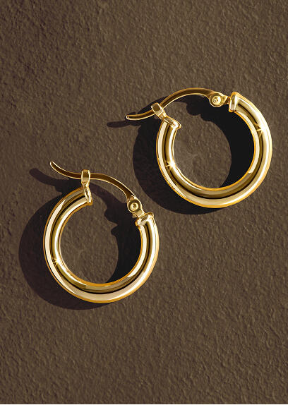 A pair of yellow gold hoop earrings shine against a brown background. 