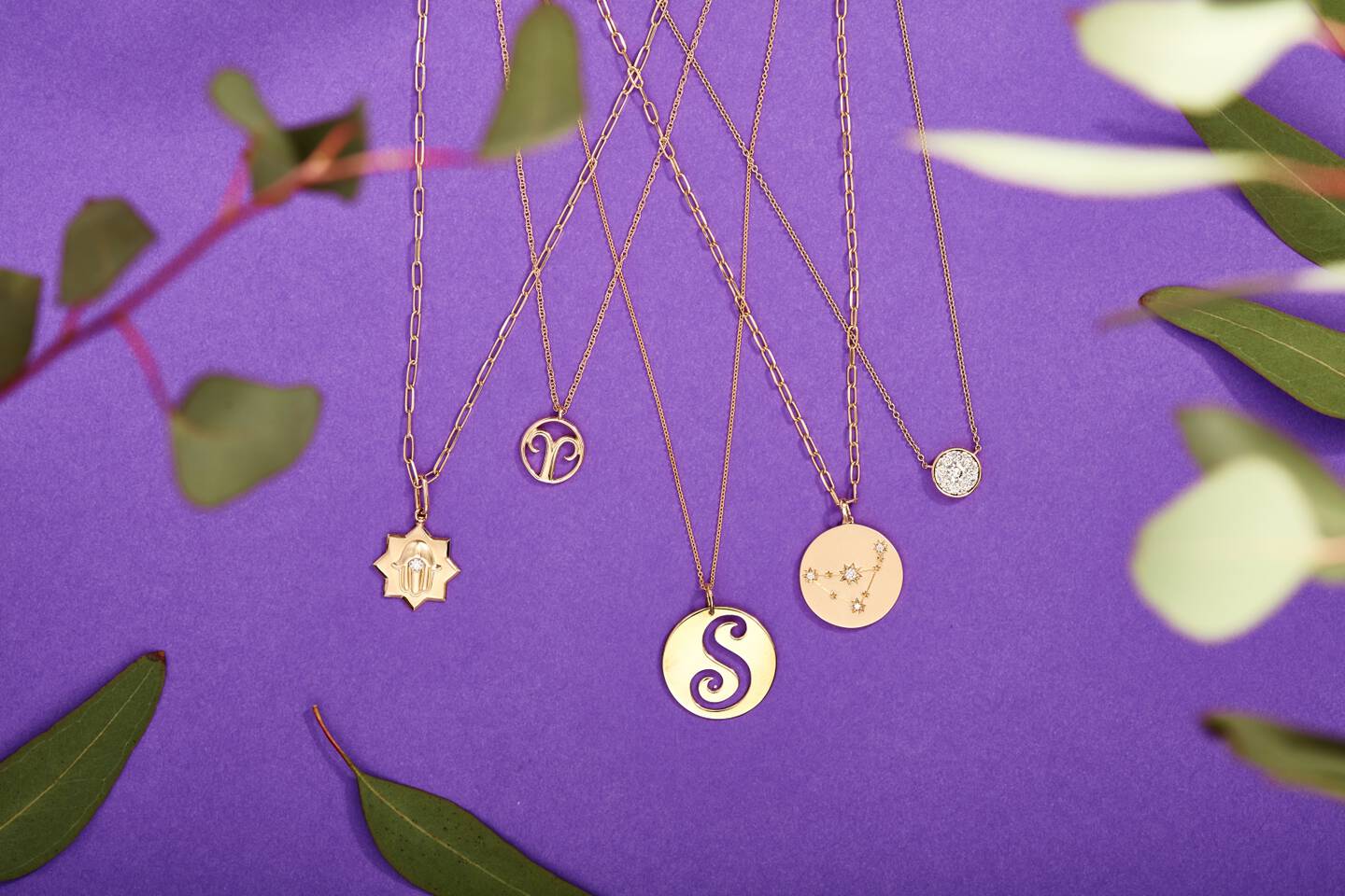 Gold and diamond pendants featuring the zodiac symbol with a purple background