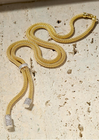 A bolo-style yellow gold necklace features white gold and diamond accents and rests on a porous stone surface.