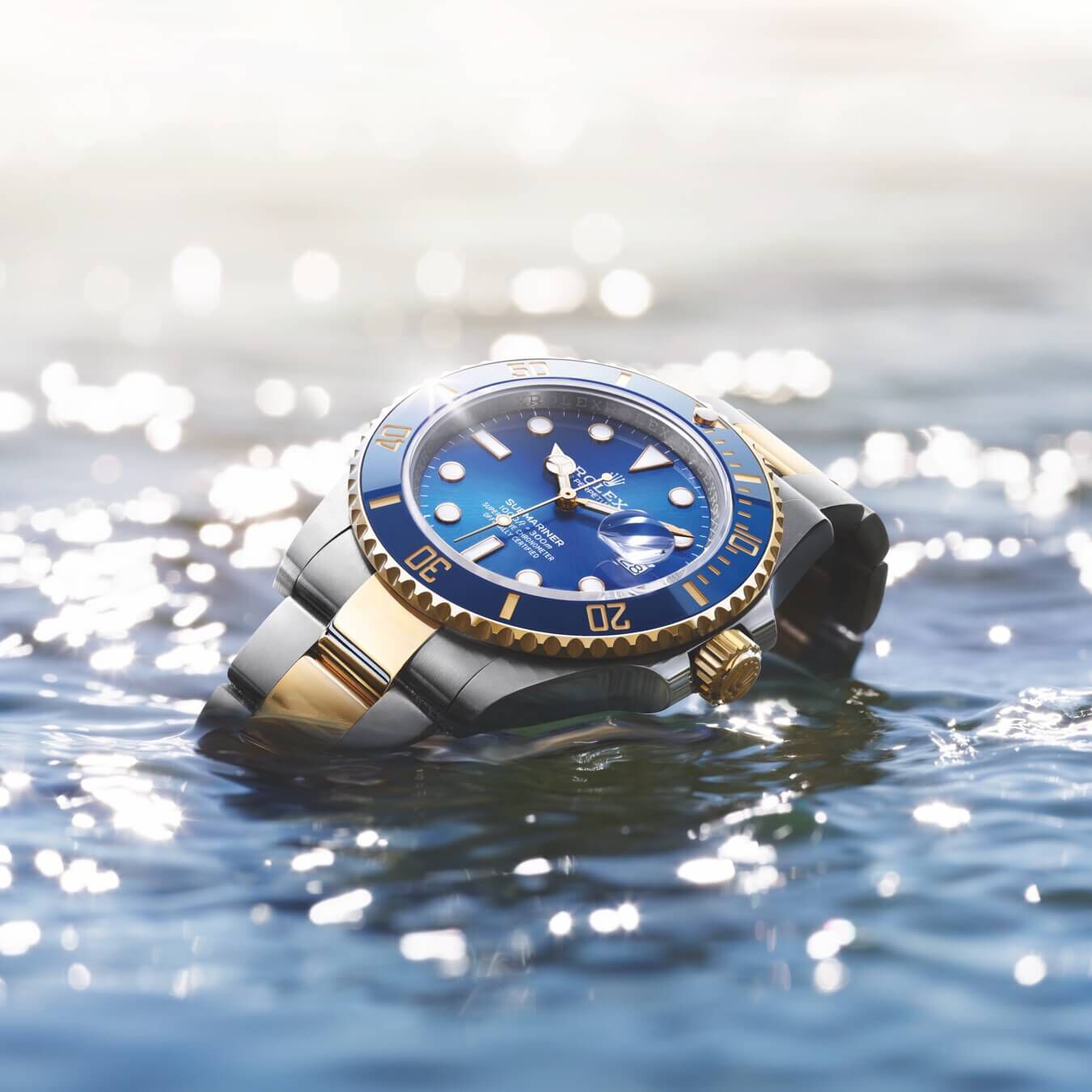 a blue and gold Rolex Submariner rises above the water