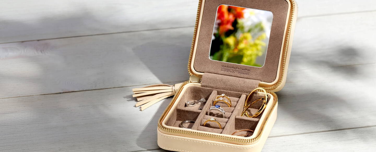 A travel sized jewelry box with gemstone rings and hoop earrings inside. 