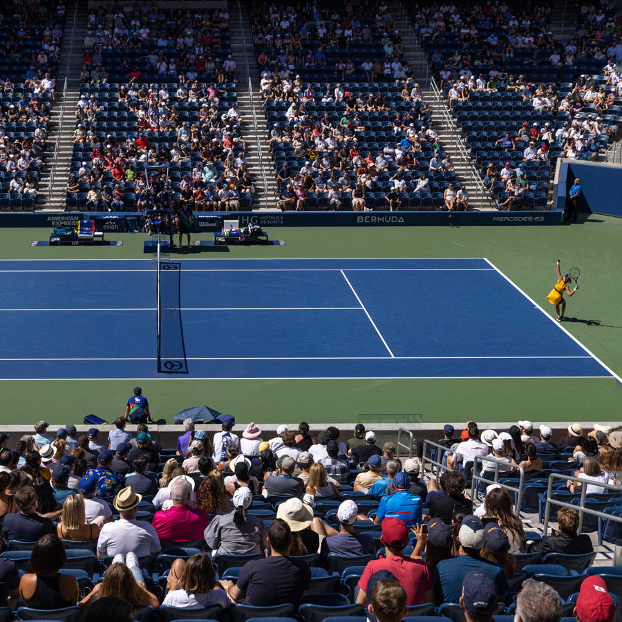 Elite tennis player reaches upward in preparation of her serve in front of a lively US Open crowd.