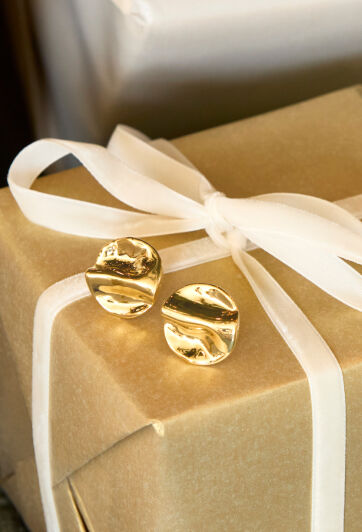 Gold studs rest atop a gift box adorned with a white ribbon. 