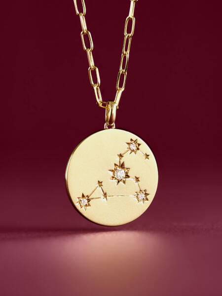 A diamond pendant necklace featuring a round disc and zodiac symbol shines in yellow gold.