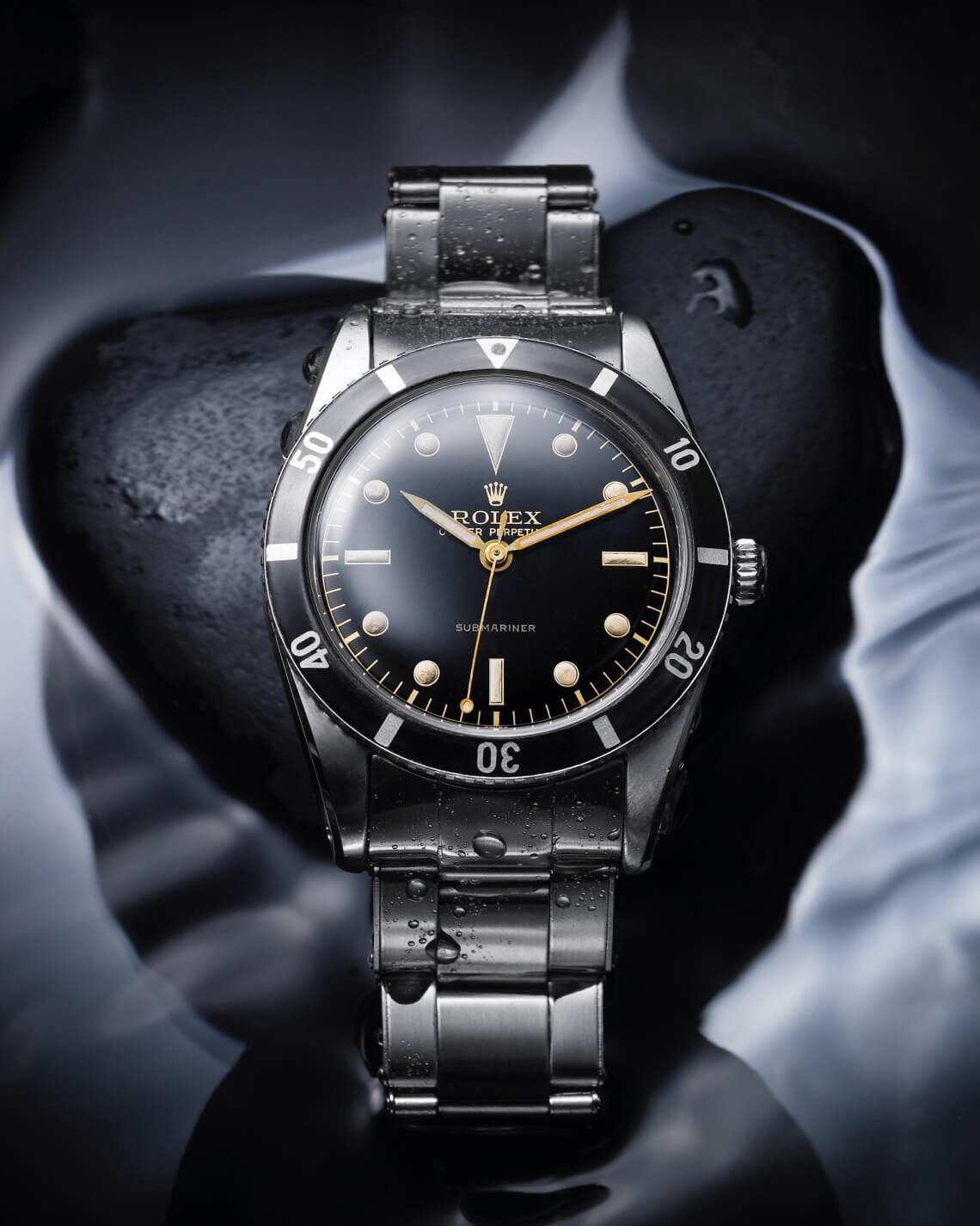 A Rolex Oyster Perpetual Submariner from 1953 against a black background with encroaching water 
