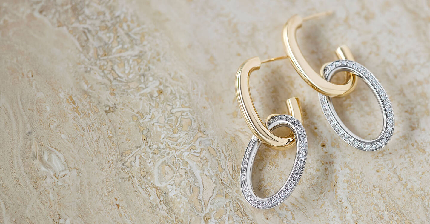 A pair of hoop earrings with oval shaped diamond settings rests on a marble tabletop.
