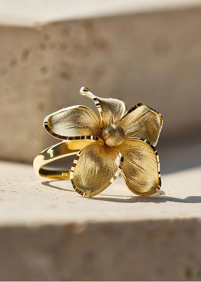 A yellow gold ring with a floral design rests on its side on a beige stone surface.