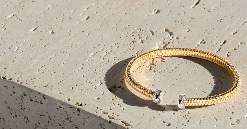 Gold Toscano cuff bracelet laying on a stone surface