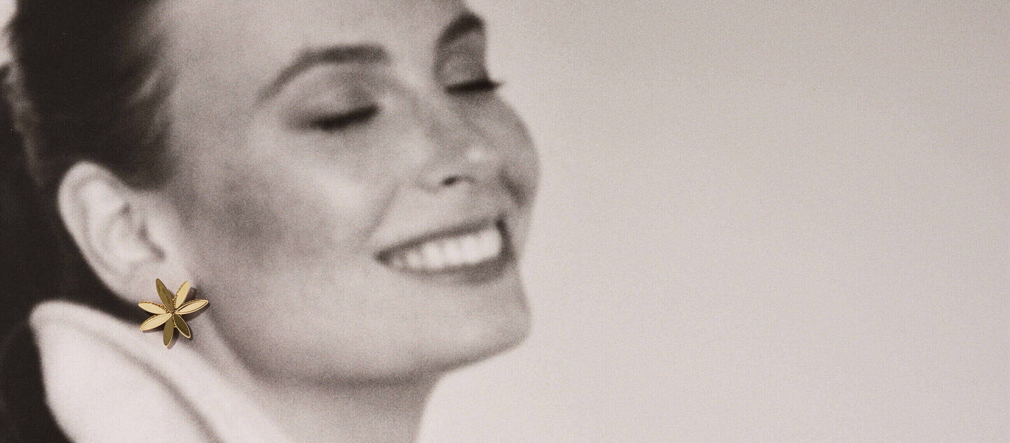 A woman is holding a gift near a tree decorated for the holiday while a dog watches.