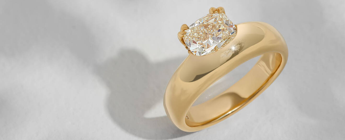 A solitaire diamond ring with an off-centered primary stone in a prong setting of yellow gold. 