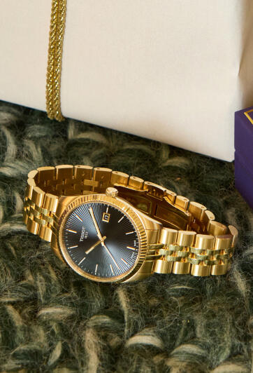 A yellow gold luxury watch rests on a marble surface