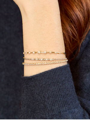 Assortment of gold chain bracelets worn on wrist.