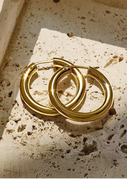A pair of classic 14k yellow gold hoops on a stone surface.