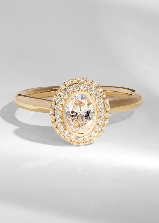 An oval cut diamond engagement ring in yellow gold with a double halo of sparkling round diamonds. 