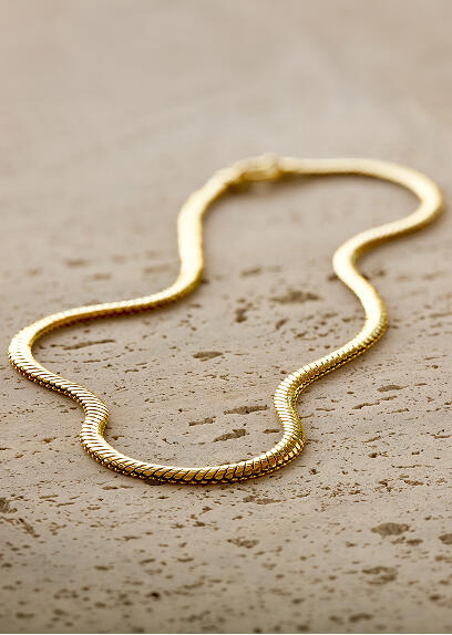 A yellow gold necklace on a beige stone surface.