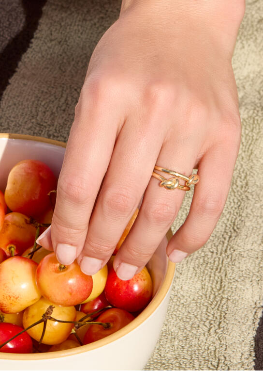 A hand reaches into a bowl of cherries