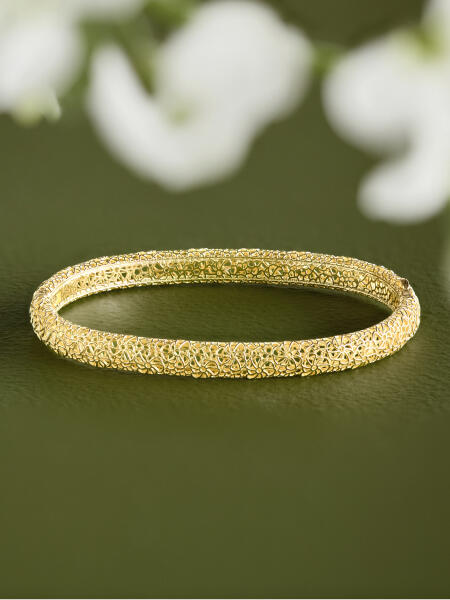 A textured yellow gold bangle on a green surface.