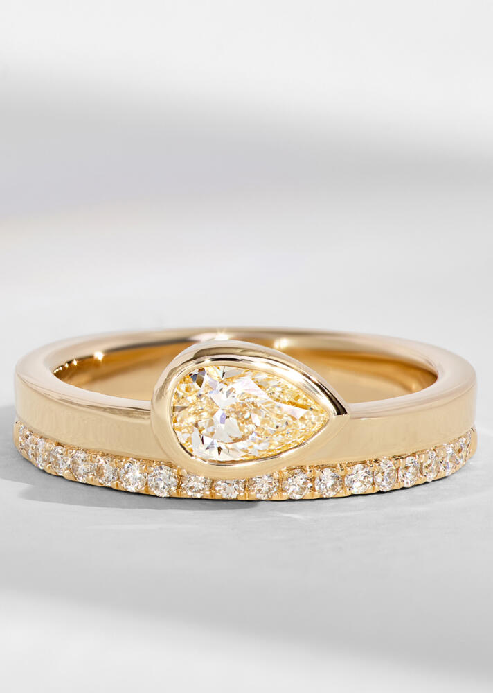 A wedding set in yellow gold with diamonds is stacked on a white surface