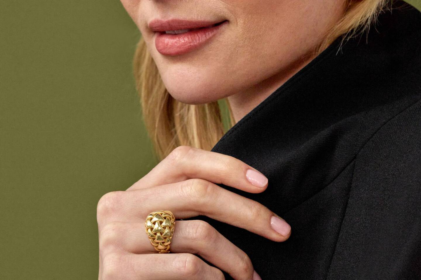 Woman wearing a yellow gold ring adjusts her shirt collar. 
