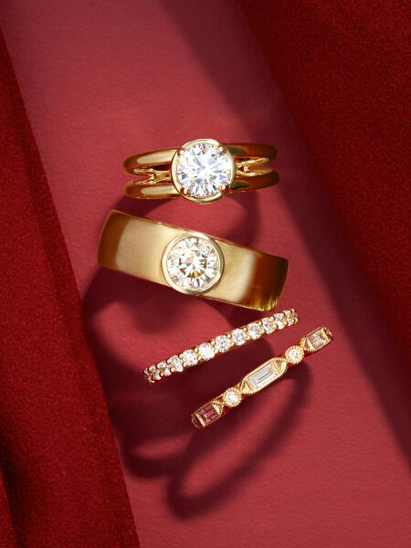 Four bridal rings in yellow gold with varying shapes of diamonds sparkle against a red background.