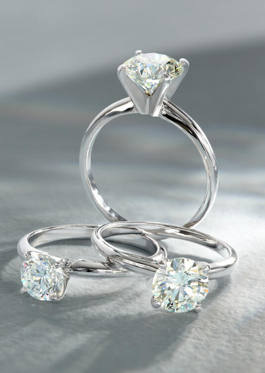 Three solitaire engagement rings, one standing and two resting on their sides, sparkle and shine in settings of 14k white gold.