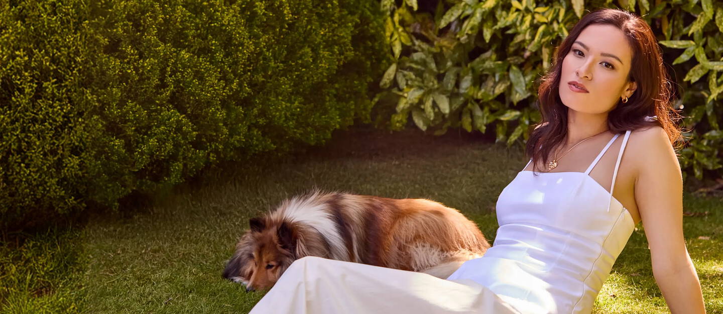 A woman with a white dress relaxes in the grass with her dog.