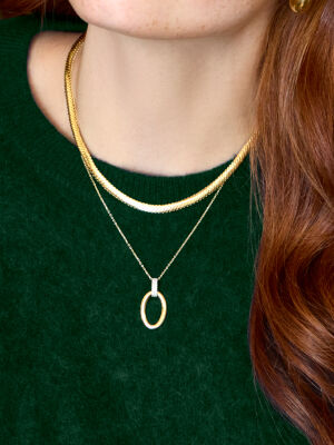 Woman in green sweater wearing two gold necklaces, one featuring an oval gold pendant with diamonds. 