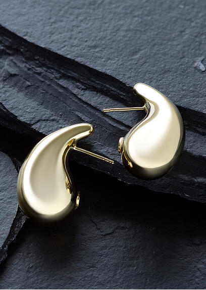 A pair of yellow gold teardrop earrings glow against a black surface.