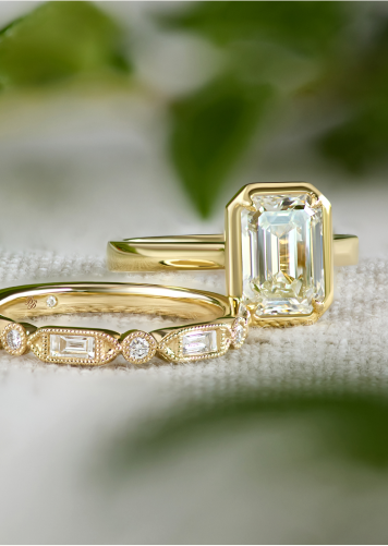 Bridal set in diamonds and 14k yellow gold resting on a fabric surface with out of focus plants in the background.