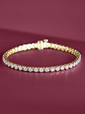 Diamond tennis bracelet set in yellow gold against a purple background.