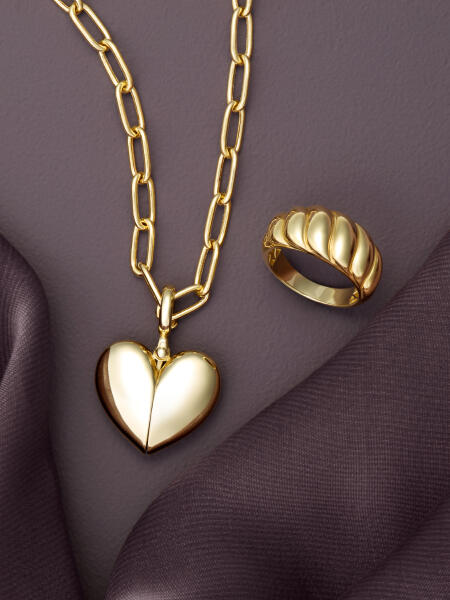 A yellow gold heart-shaped pendant necklace and a yellow gold ring reflect the light on a purple surface.&nbsp;