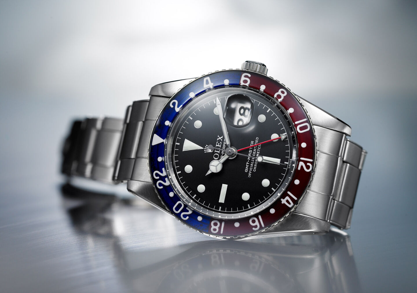 Rolex GMT-Mater with black dial and Pepsi bezel against a silver background. 