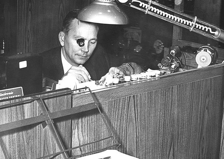 Historical black and white image of man wearing a loupe, inspecting jewelry 