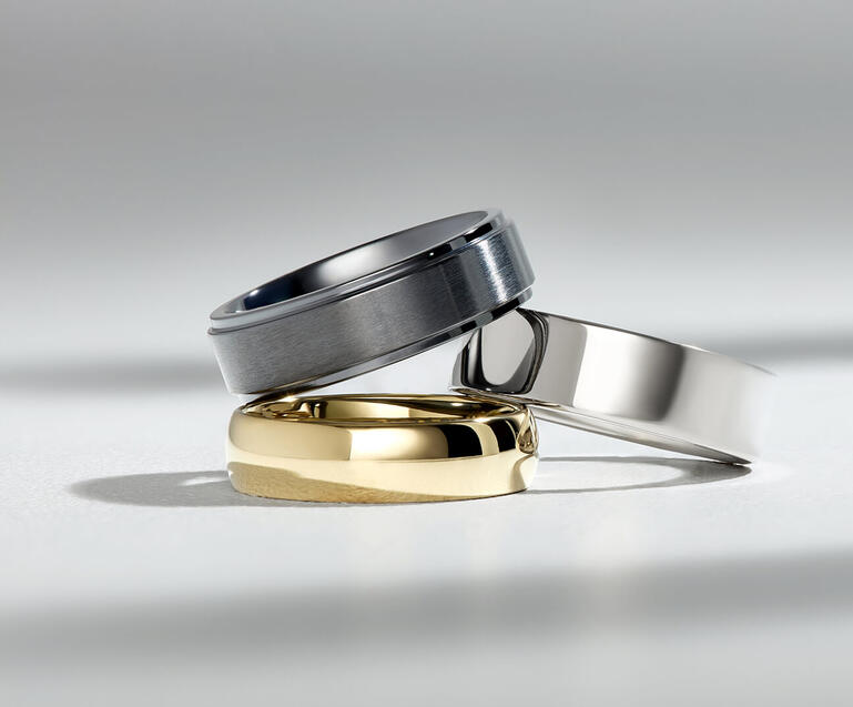 A stack of custom men&rsquo;s wedding bands in a variety of precious metals and customization options. 