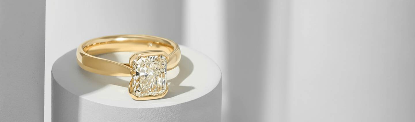 Fancy shaped diamond ring in yellow gold rests on a round pedestal