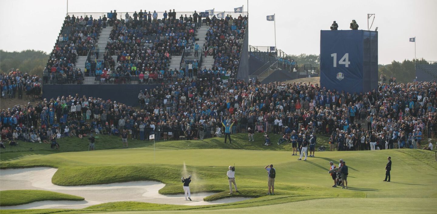 Golfer takes a swing from the sand trap in front of a large crowd at the Ryder Cup. 