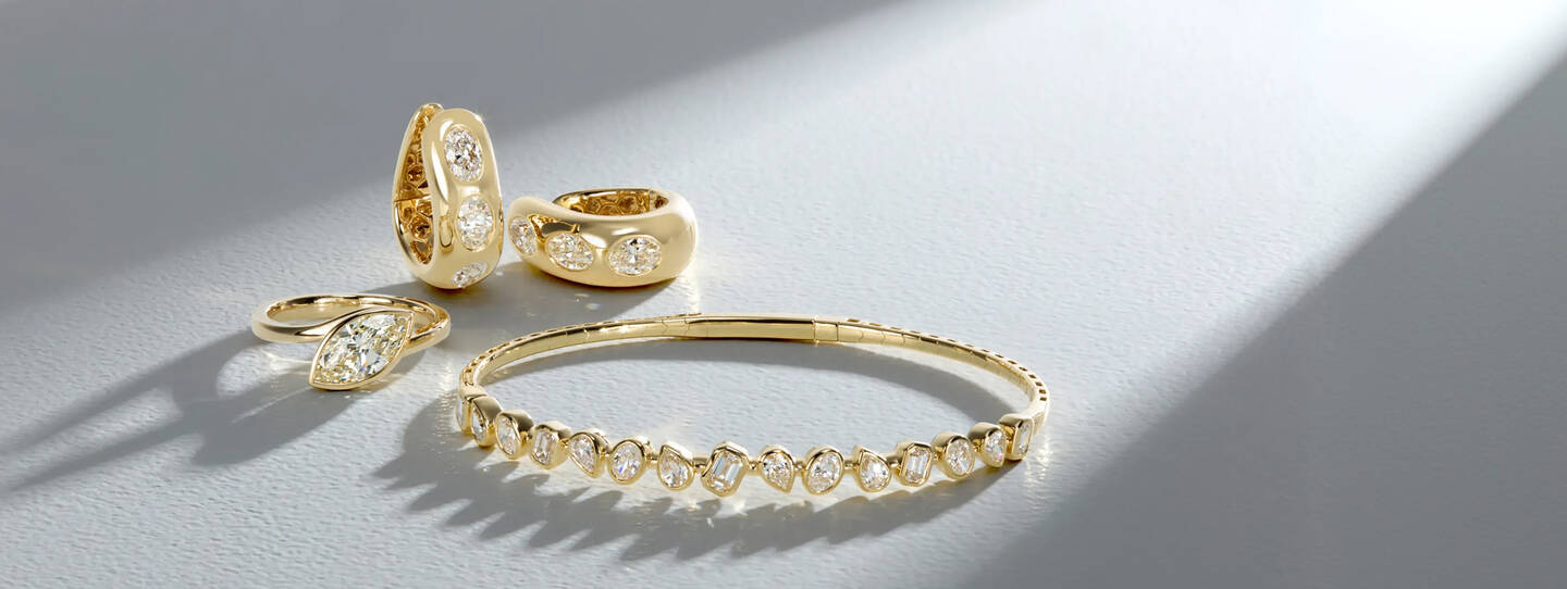 Diamond jewelry, including a ring, earrings and bracelet crafted in yellow gold shine on a surface of light gray.