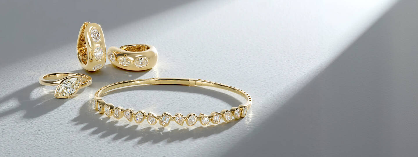 Diamond jewelry, including a ring, earrings and bracelet crafted in yellow gold shine on a surface of light gray. 