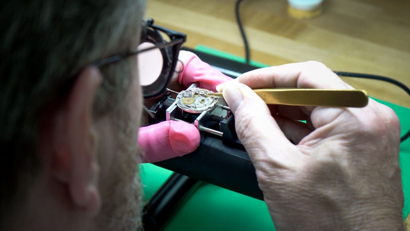 A watchmaker at his desk working on a complex luxury watch movement.
