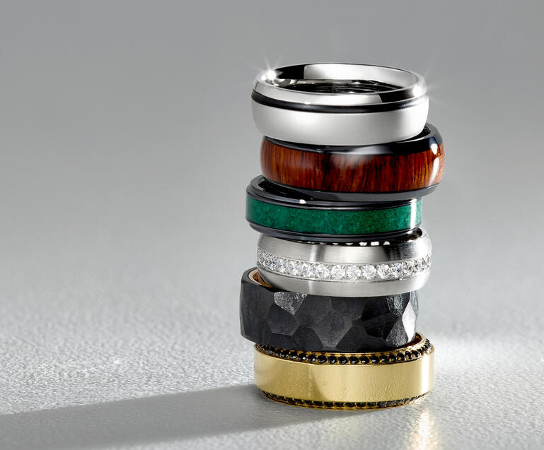 A stack of custom men&rsquo;s wedding bands in a variety of precious metals and customization options.