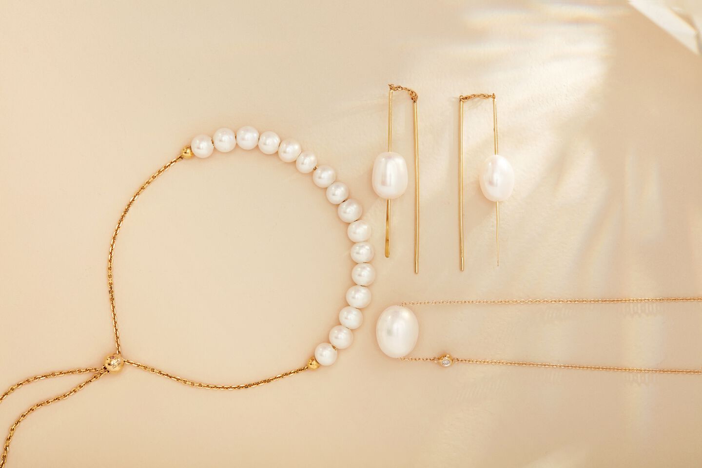 Pearl earrings, necklace and bracelet displayed in 14k yellow gold with an off-white background. 