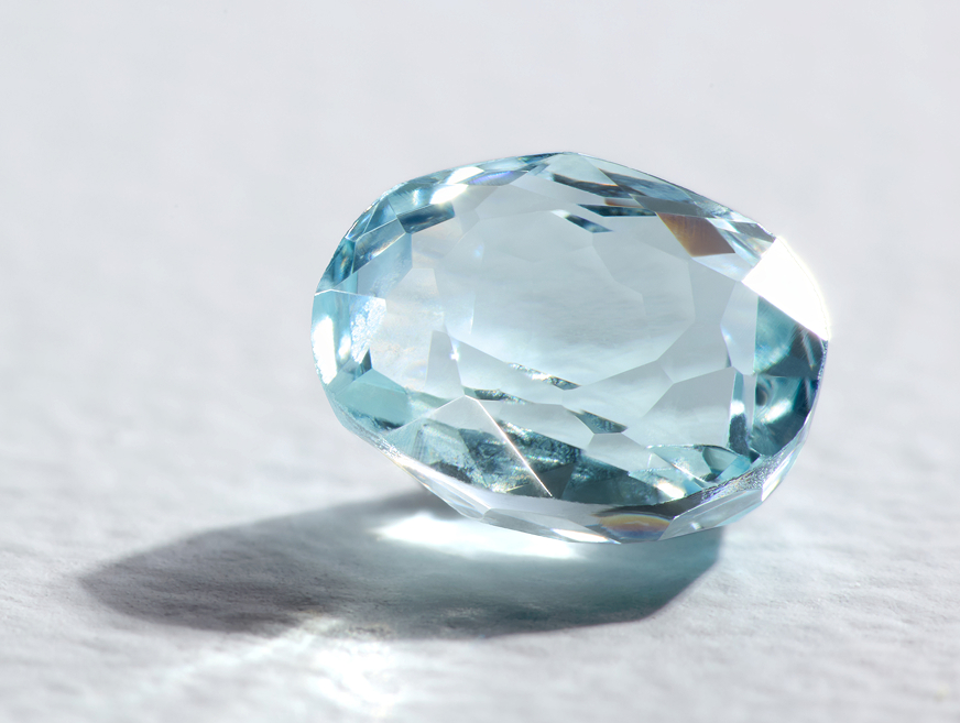 A natural aquamarine gemstone reflects on a textured off-white surface.