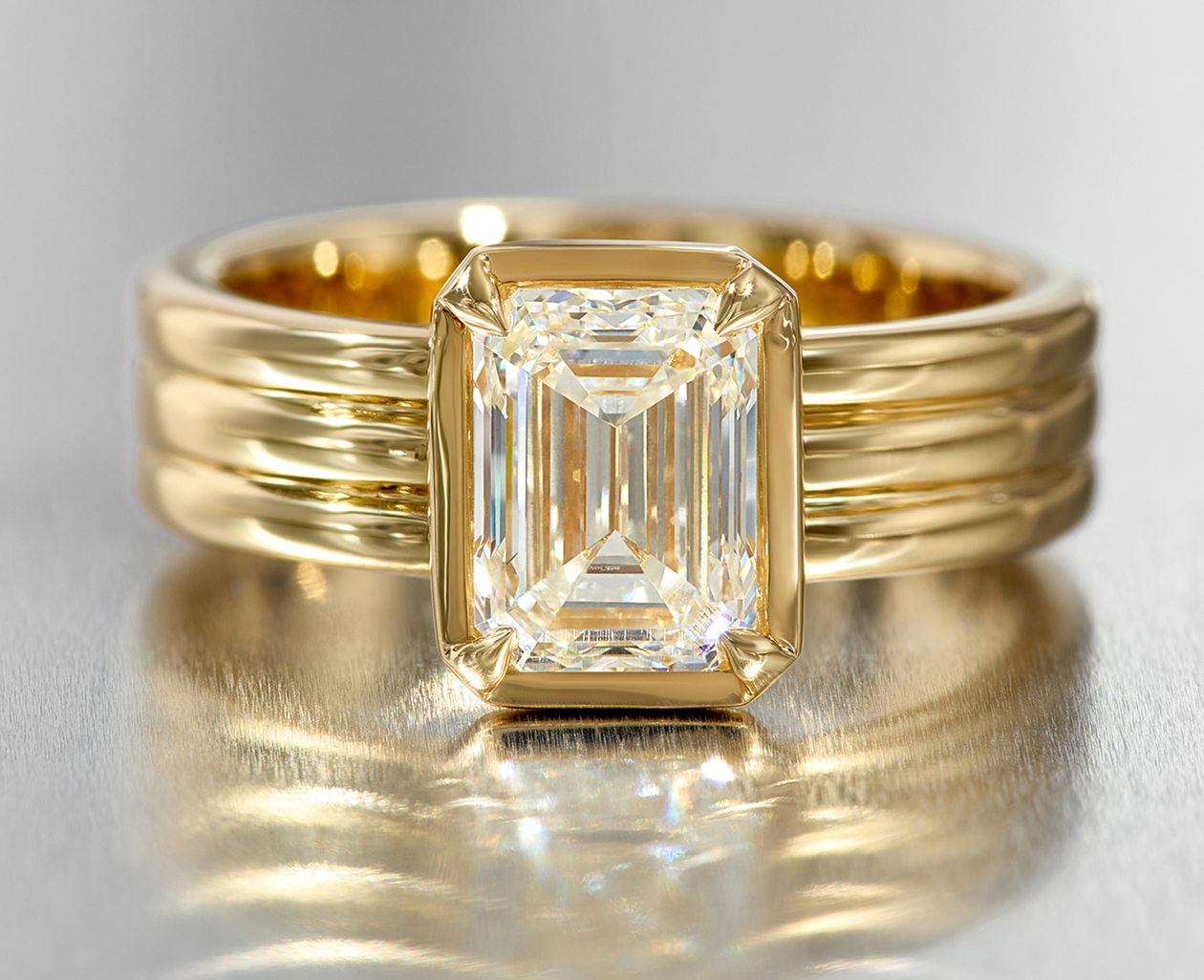 A solitaire diamond engagement ring with a three-row band and bezel 
set emerald cut diamond.