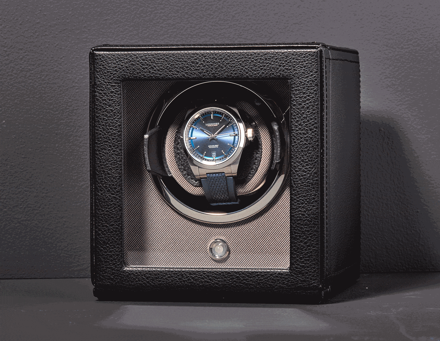 A watch with a blue dial inside an automatic watch winder with a black leather exterior.
